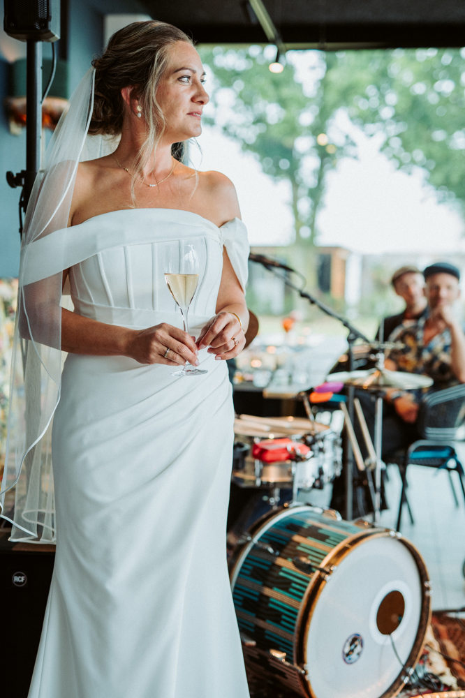 Real-Bride-Revie-bruidszaak-janneke-krancher-foto1-Bruid in moderne off-shoulder trouwjurk met plooidetail tijdens toast op bruiloft - Bruidshuis Diana
